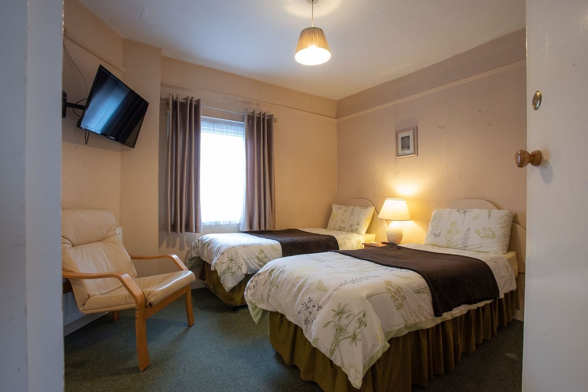 A hotel room with two beds, a chair, a television mounted on the wall, and a window with curtains.