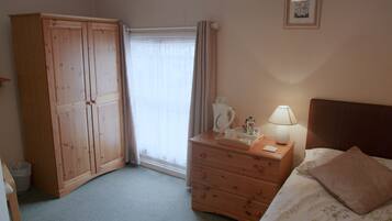 A bedroom with a wooden wardrobe, a bedside table with a lamp, a bed with a floral bedspread, and a window with curtains.