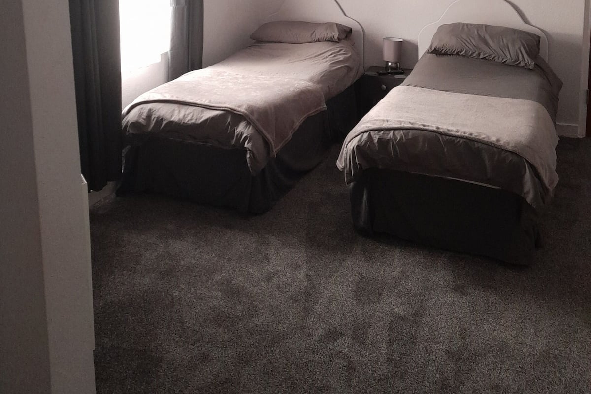 A small, dimly lit room with two single beds, a small table, and a hanging light fixture.