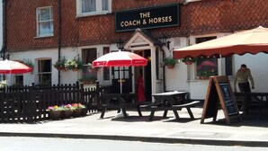 Un pub appelé « The Coach & Horses », doté d’une terrasse et de parasols rouges.