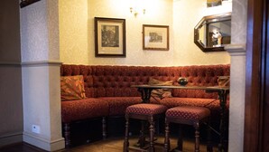 Un coin salon avec un banc rembourré et deux tabourets de bar, une petite table et des tableaux encadrés au mur.