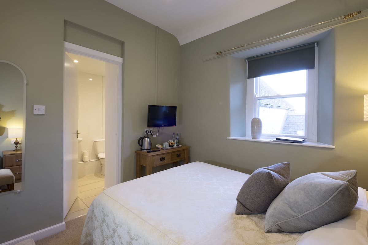 A bedroom with a bed, bedside table, TV, and a window with a view.