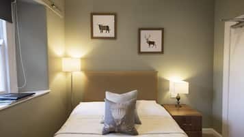 Una cama bien hecha con un cojín, una lámpara de noche y dos cuadros en la pared.