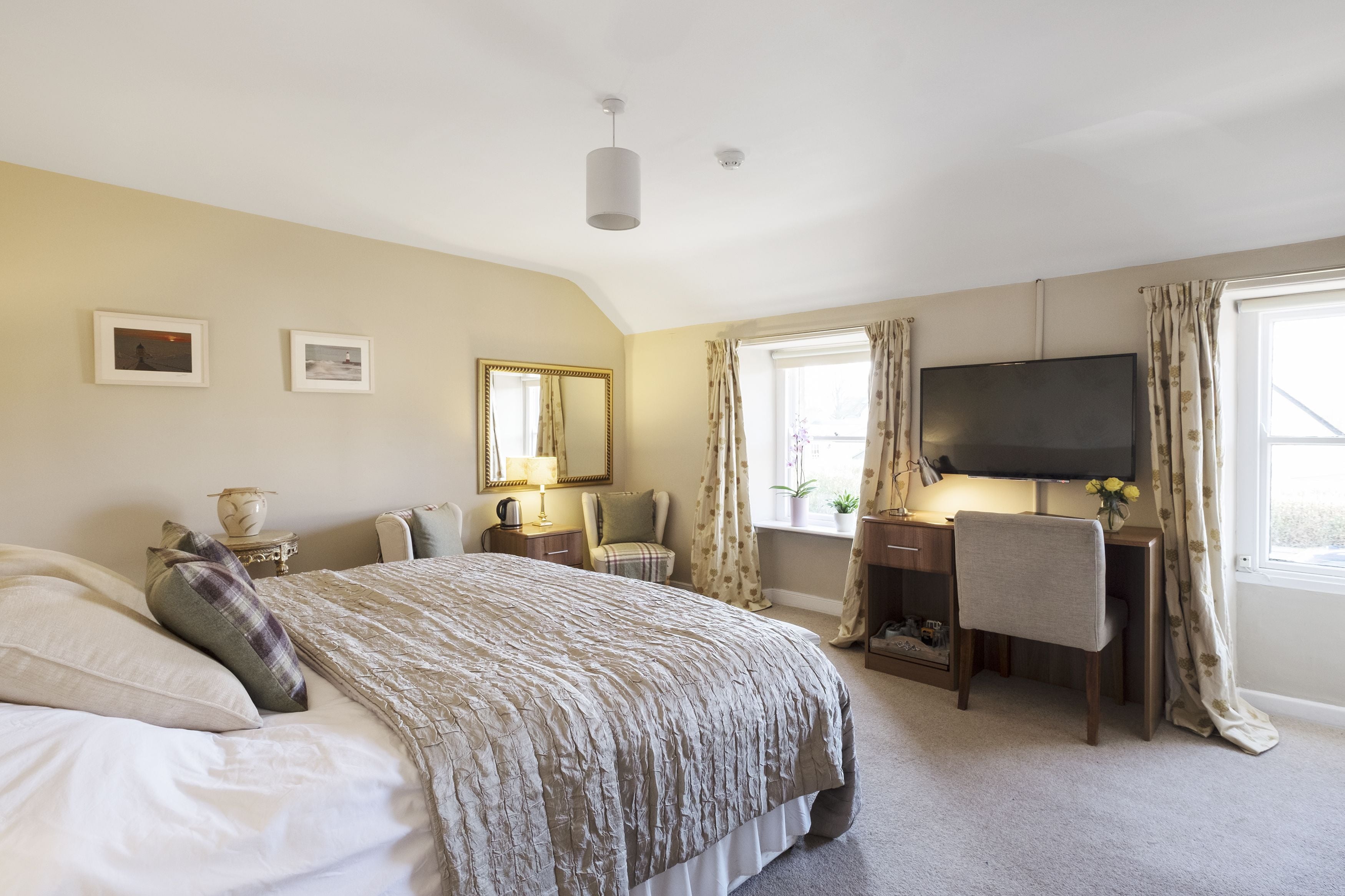 A bedroom with a bed, a desk, a chair, a TV, and a window with curtains.