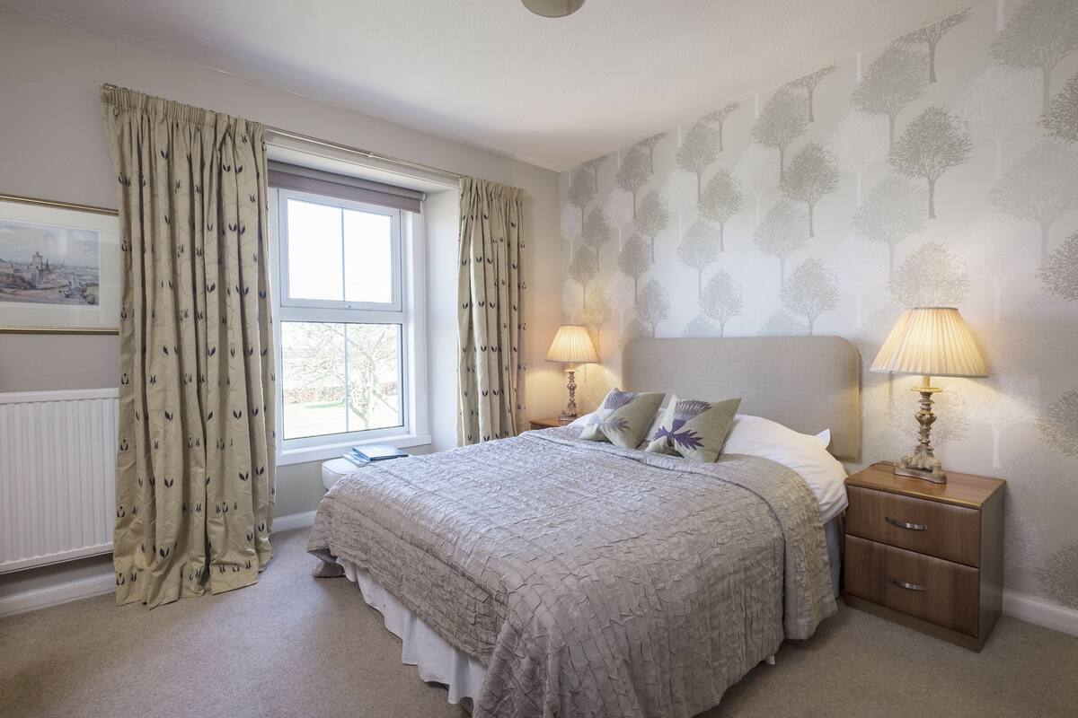 A bedroom with a bed, two bedside lamps, a nightstand, and a window with curtains.