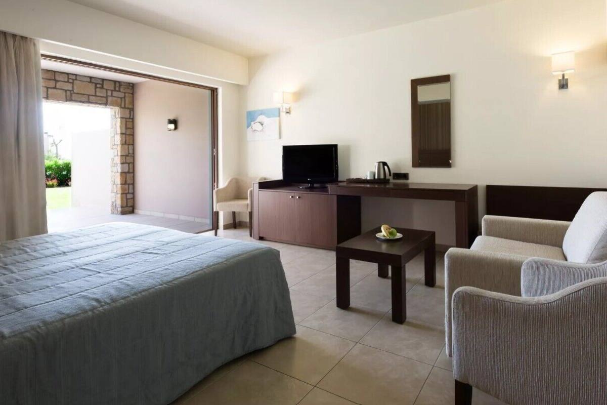 Habitació d'hotel amb un llit, un escriptori, una cadira, un televisor i una taula petita.