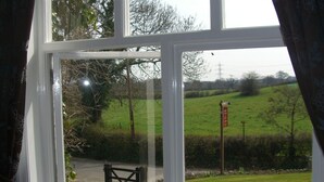 A window with a view of a rural landscape, including a grassy field, a gate, and a road. - Ash Farm Country Guest House (Altrincham)