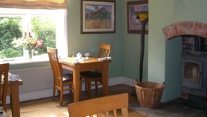 A cozy dining area with a table and chairs, a window with a view of greenery, and a wood-burning stove. - Ash Farm Country Guest House (Altrincham)