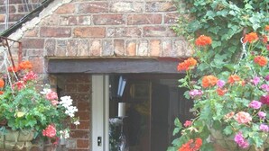 A brick building entrance with a door, surrounded by hanging flower baskets with red and pink flowers. - Ash Farm Country Guest House (Altrincham)
