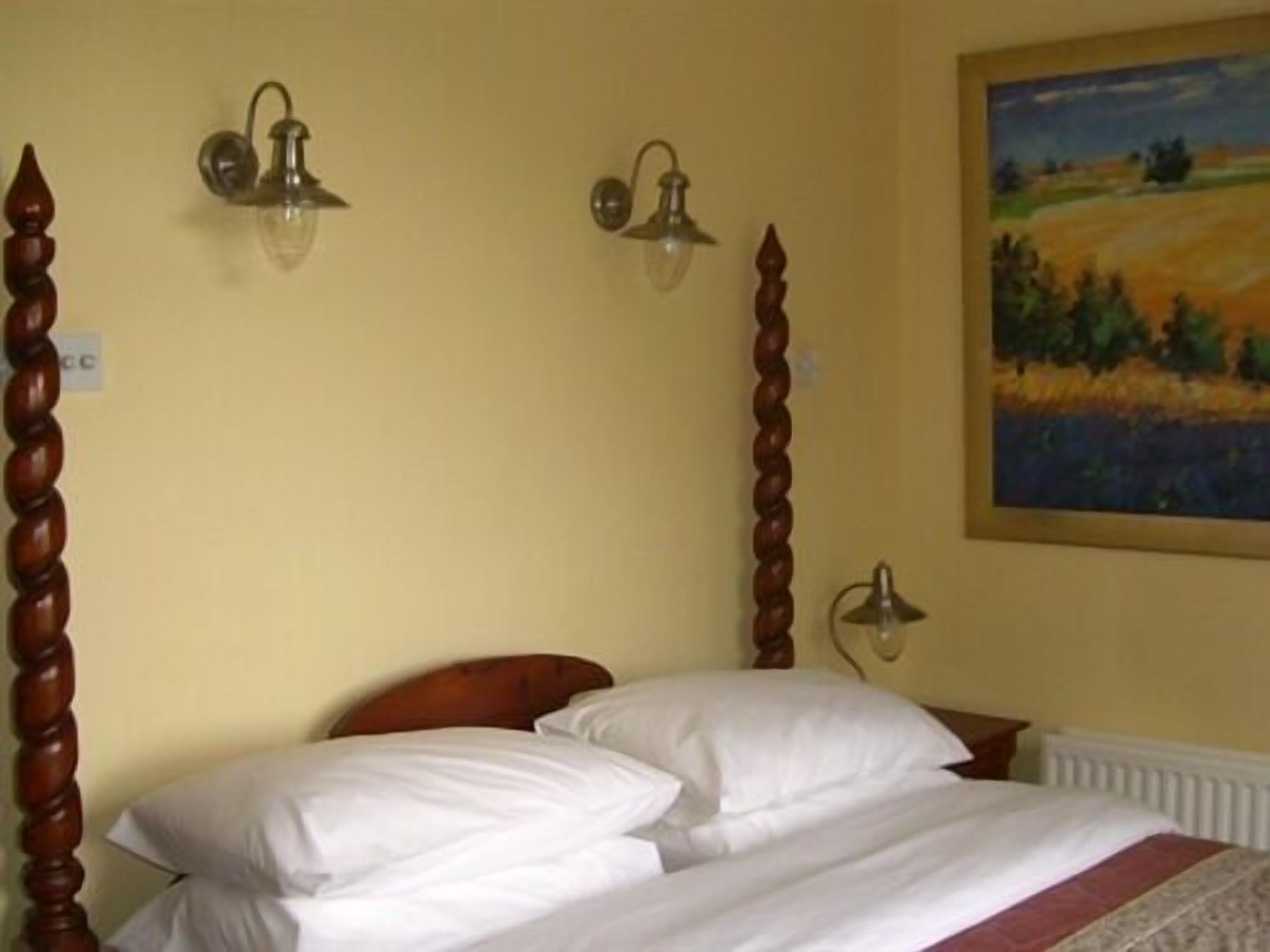 A bedroom with a wooden four-poster bed, two wall-mounted lamps, and a landscape painting on the wall.