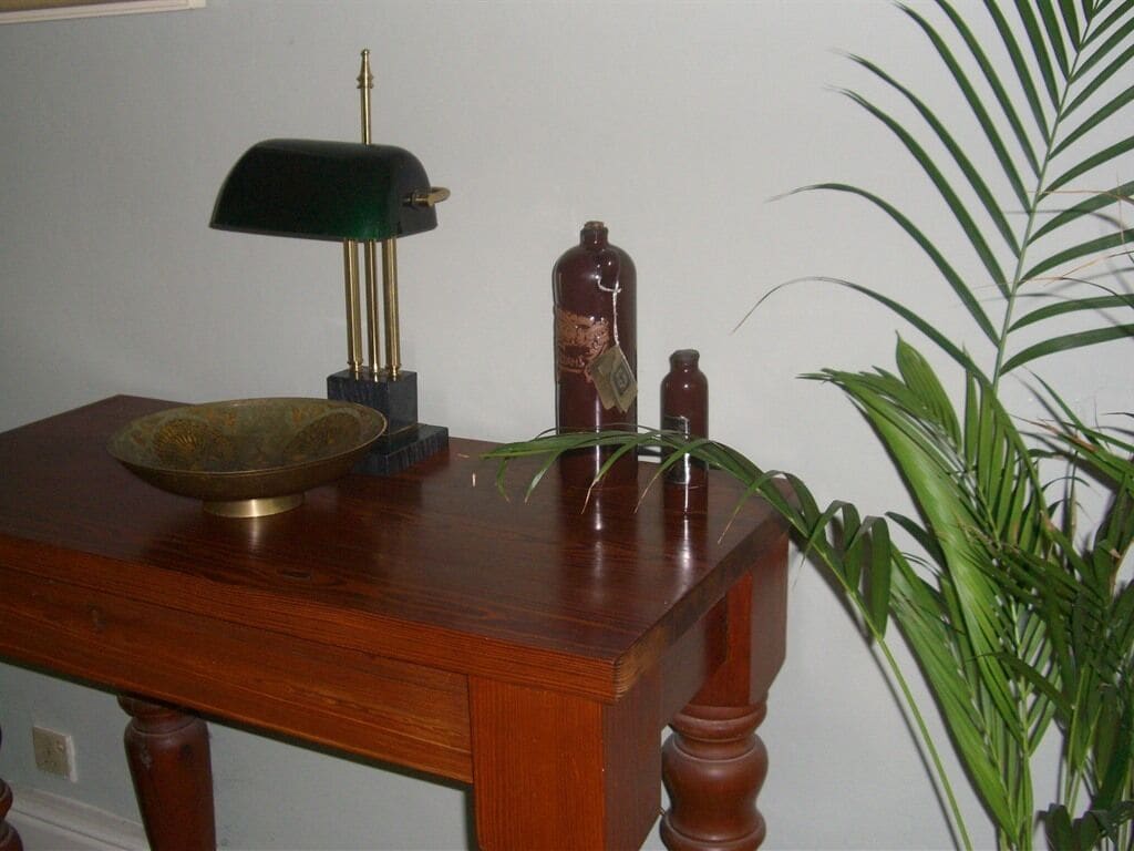 A wooden table with a green lamp, a brass bowl, and two bottles.