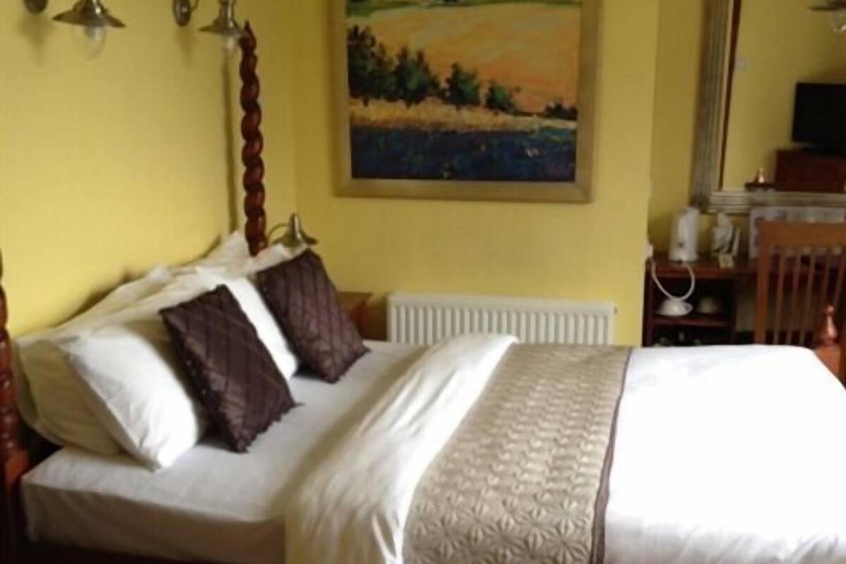 A bedroom with a bed, a painting on the wall, and a desk with a chair.