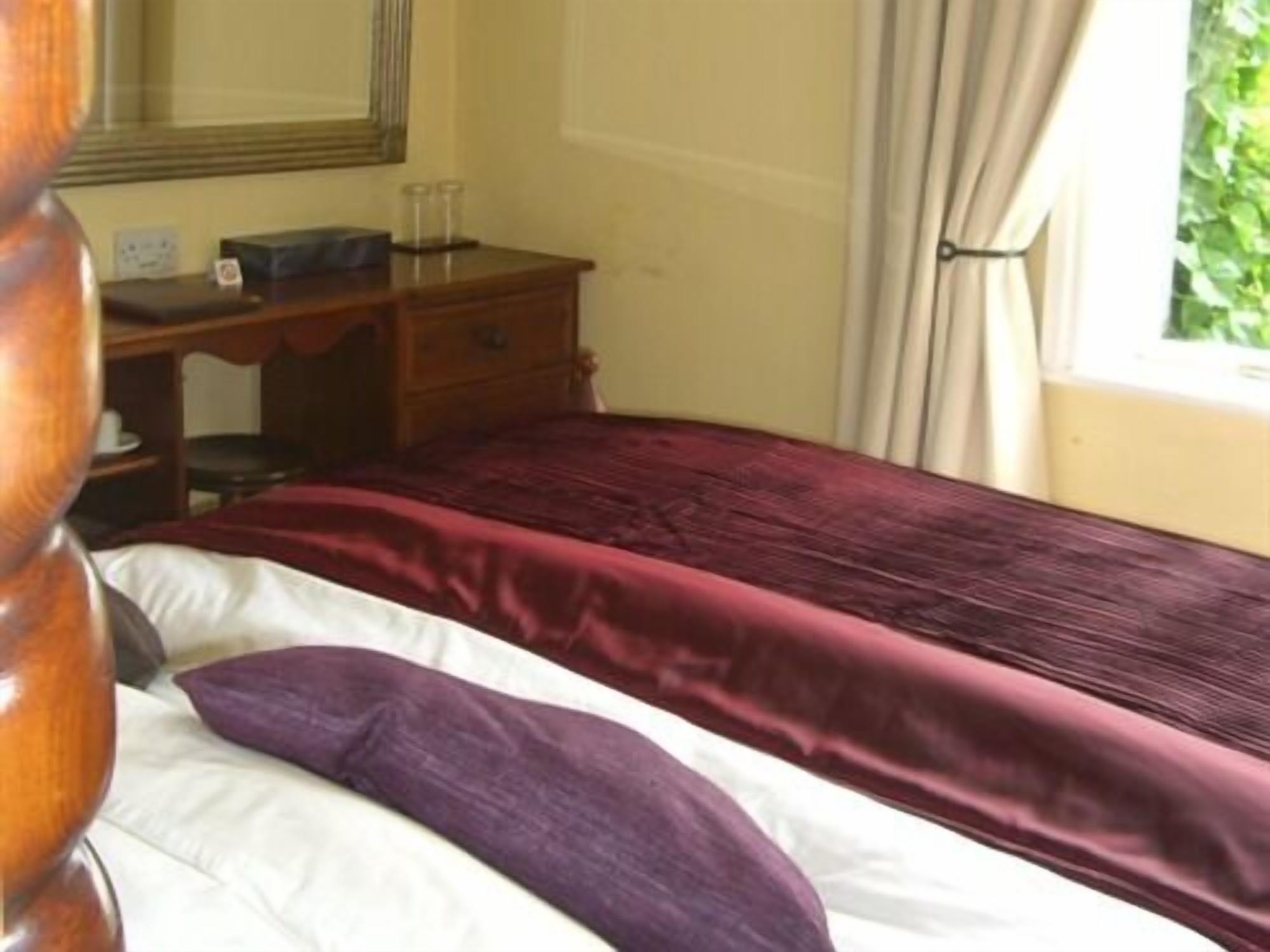 A bedroom with a bed, a wooden dresser, a mirror, and a window with curtains.