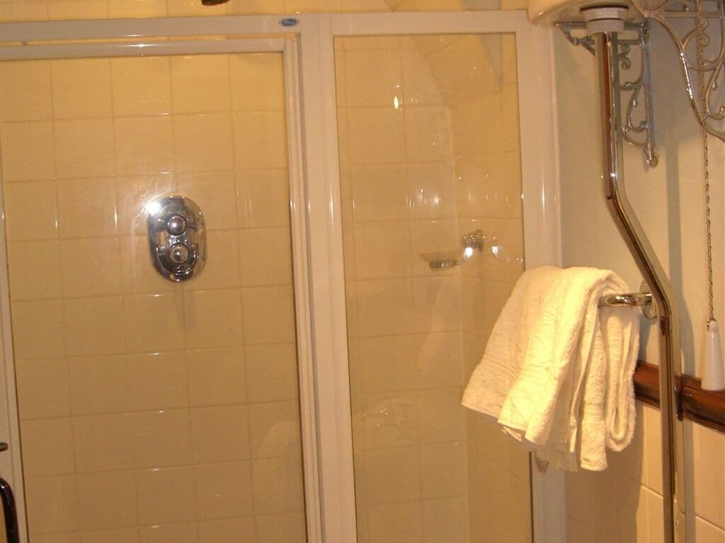 Chuveiro com porta de vidro, um porta-toalhas com uma toalha e um chuveiro cromado.
