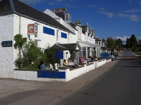 A row of white buildings with a blue sign for the Car Park and a blue sign for the Car Inn Hotel. - Cairn Hotel (Carrbridge)