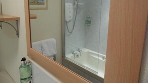 Een badkamer met een douchecabine van glas, een witte badkuip, een houten plankje met een afbeelding in een lijst, en een fles shampoo.