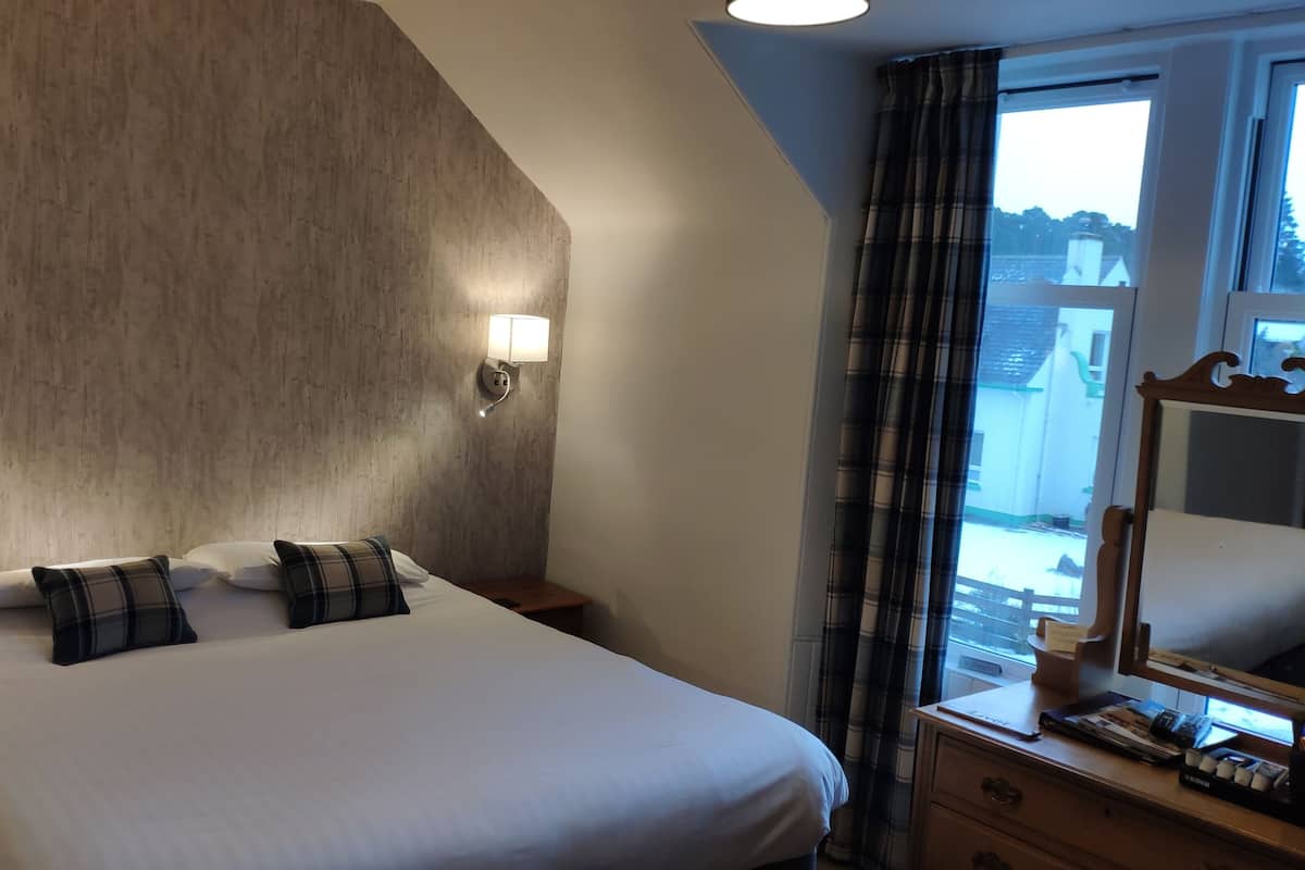 A bedroom with a large bed, two bedside lamps, a nightstand, a dresser, a mirror, and a window with curtains.