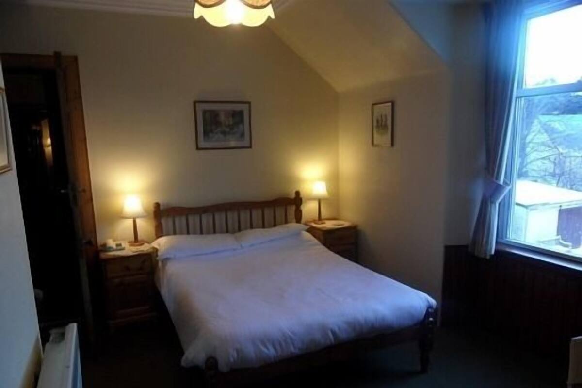 A bedroom with a single bed, two bedside tables with lamps, a ceiling light fixture, and a window with curtains.