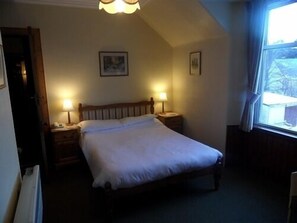 A bedroom with a single bed, two bedside tables with lamps, a ceiling light fixture, and a window with curtains.