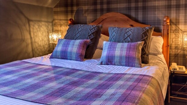 Een knus slaapkamer met een geruit sprei, een houten hoofdbord en een nachtkastje met een lamp en telefoon.
