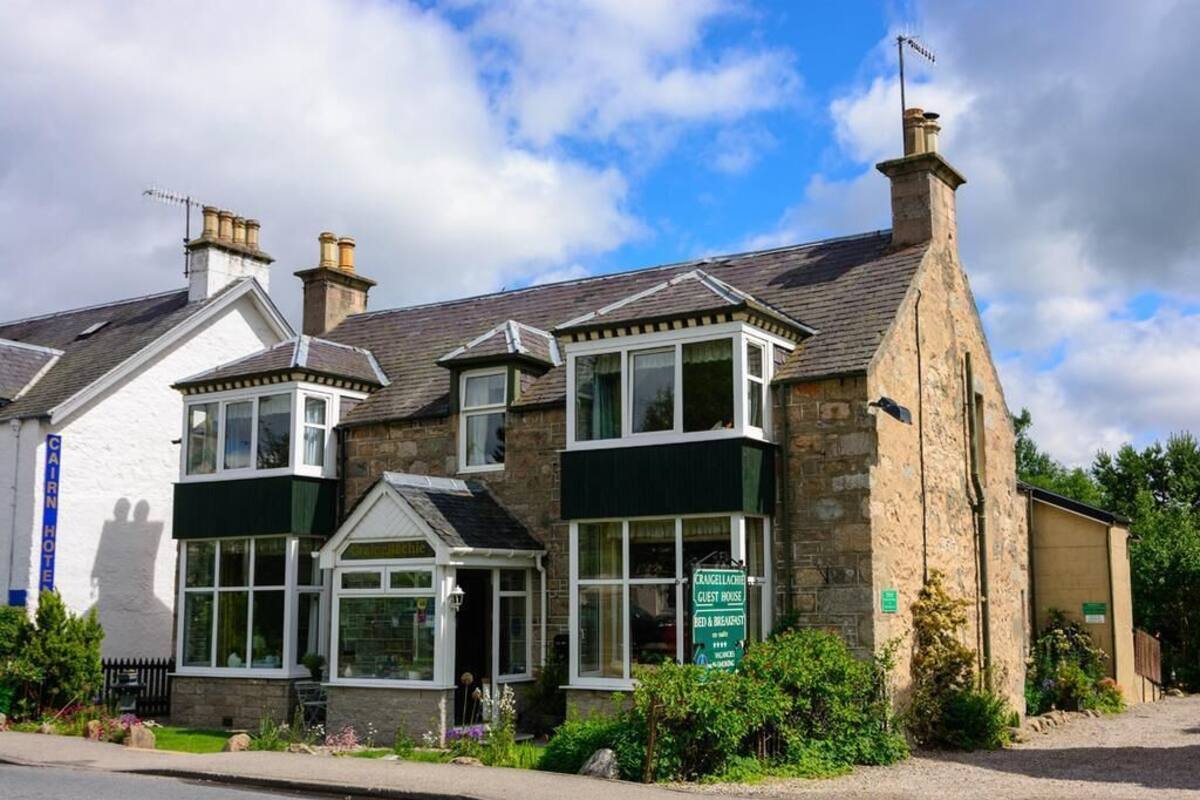 A two-story building with a stone facade, a green awning, and a sign indicating it is a guest house.