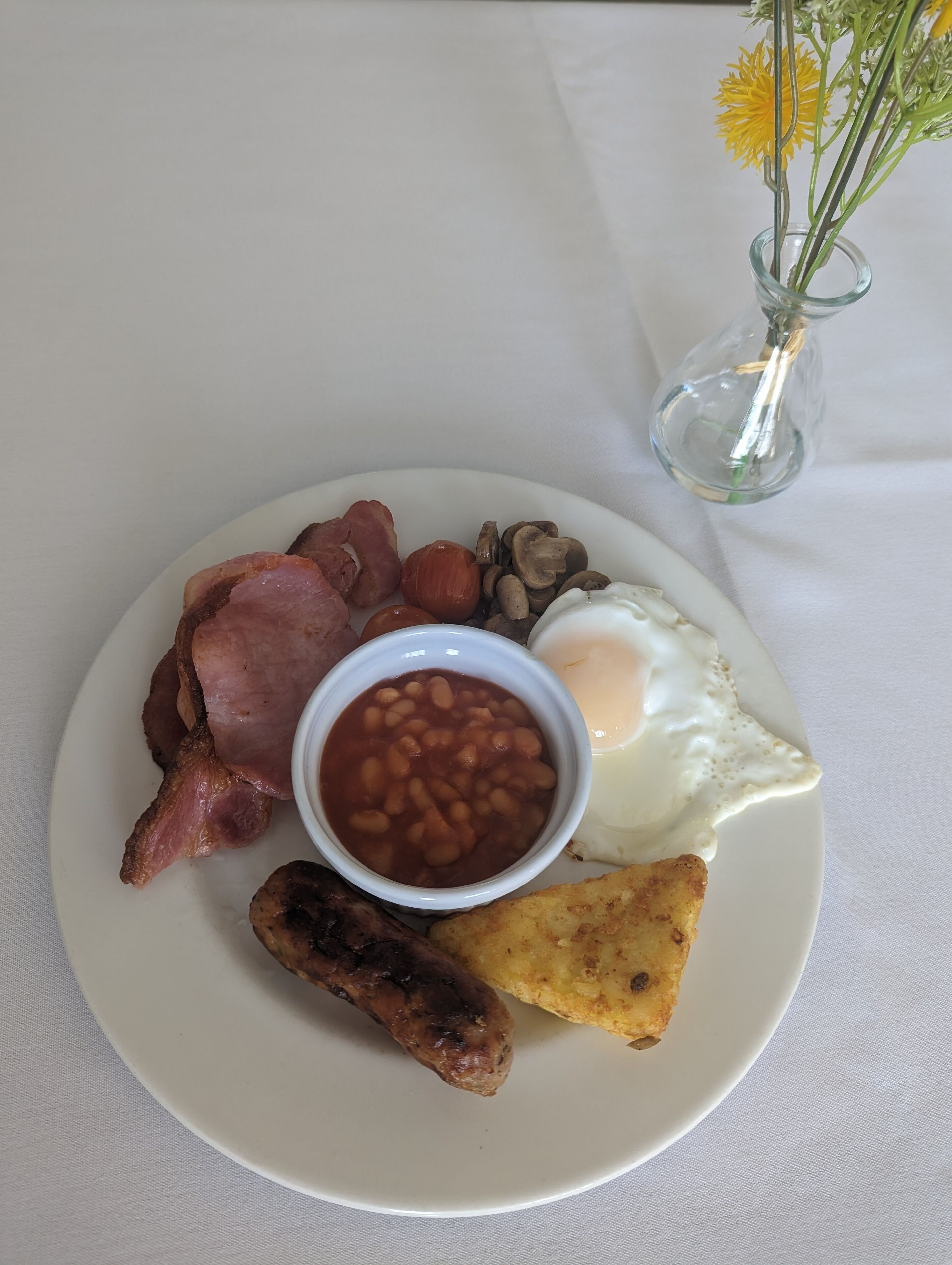 A plate of breakfast food including bacon, beans, eggs, mushrooms, and sausages.