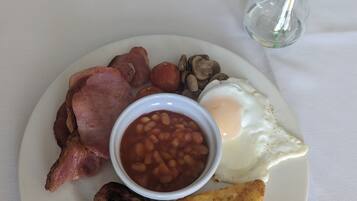 A plate of breakfast food including bacon, beans, eggs, mushrooms, and sausages.