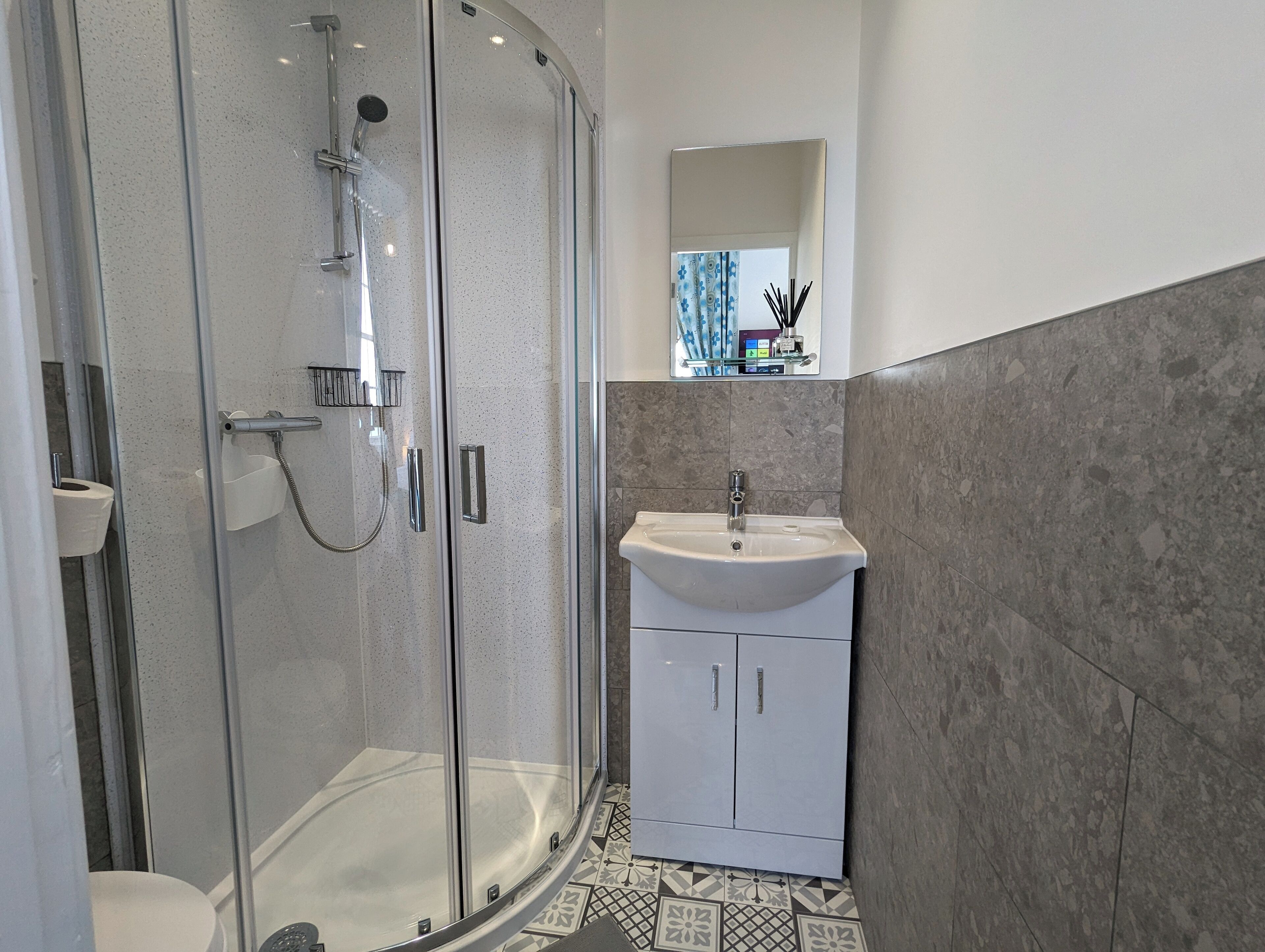 A modern bathroom with a glass-enclosed shower, a white sink, and a tiled floor.
