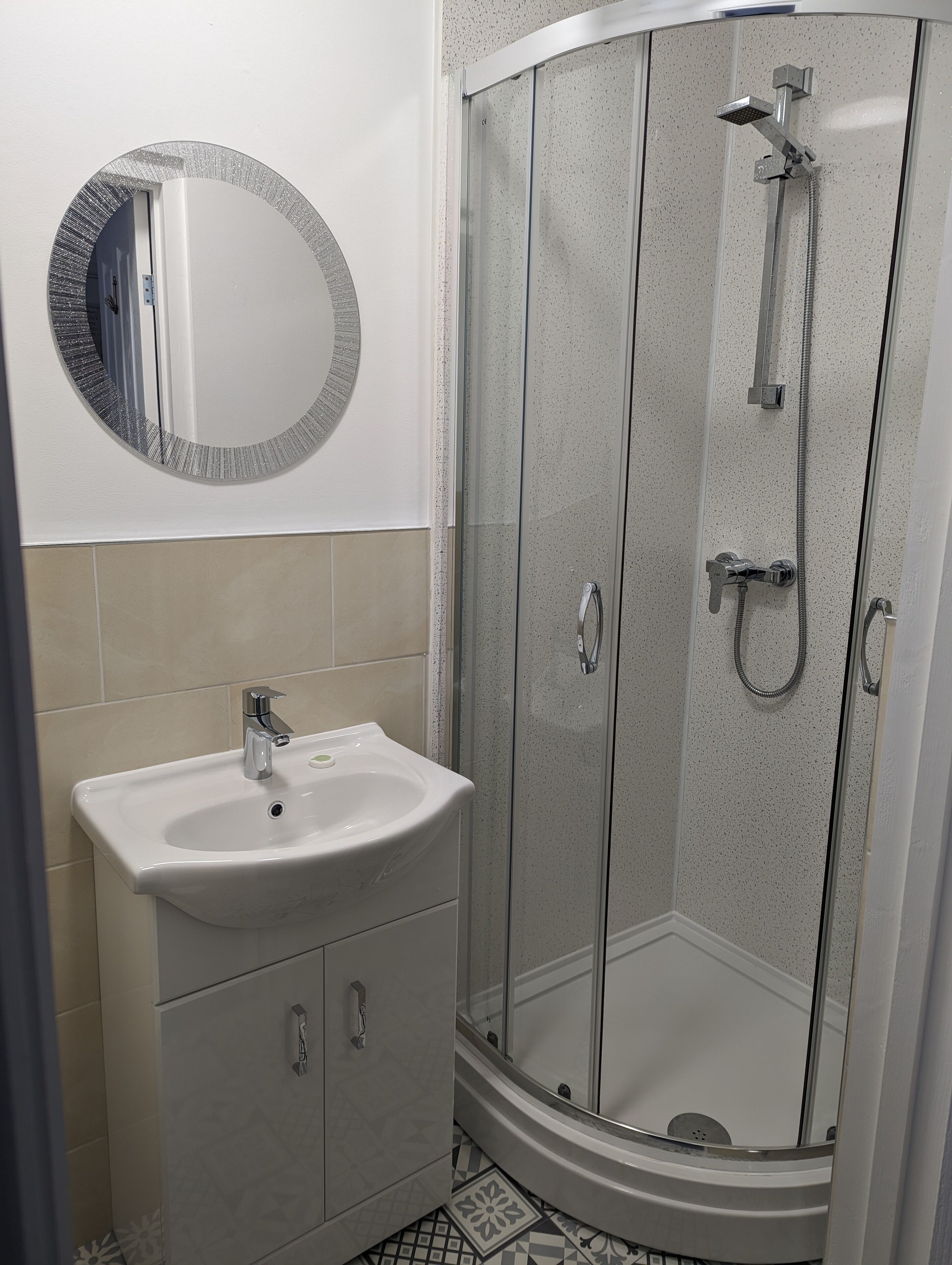 Un baño con un lavamanos blanco, un espejo redondo y una ducha con mampara de vidrio.