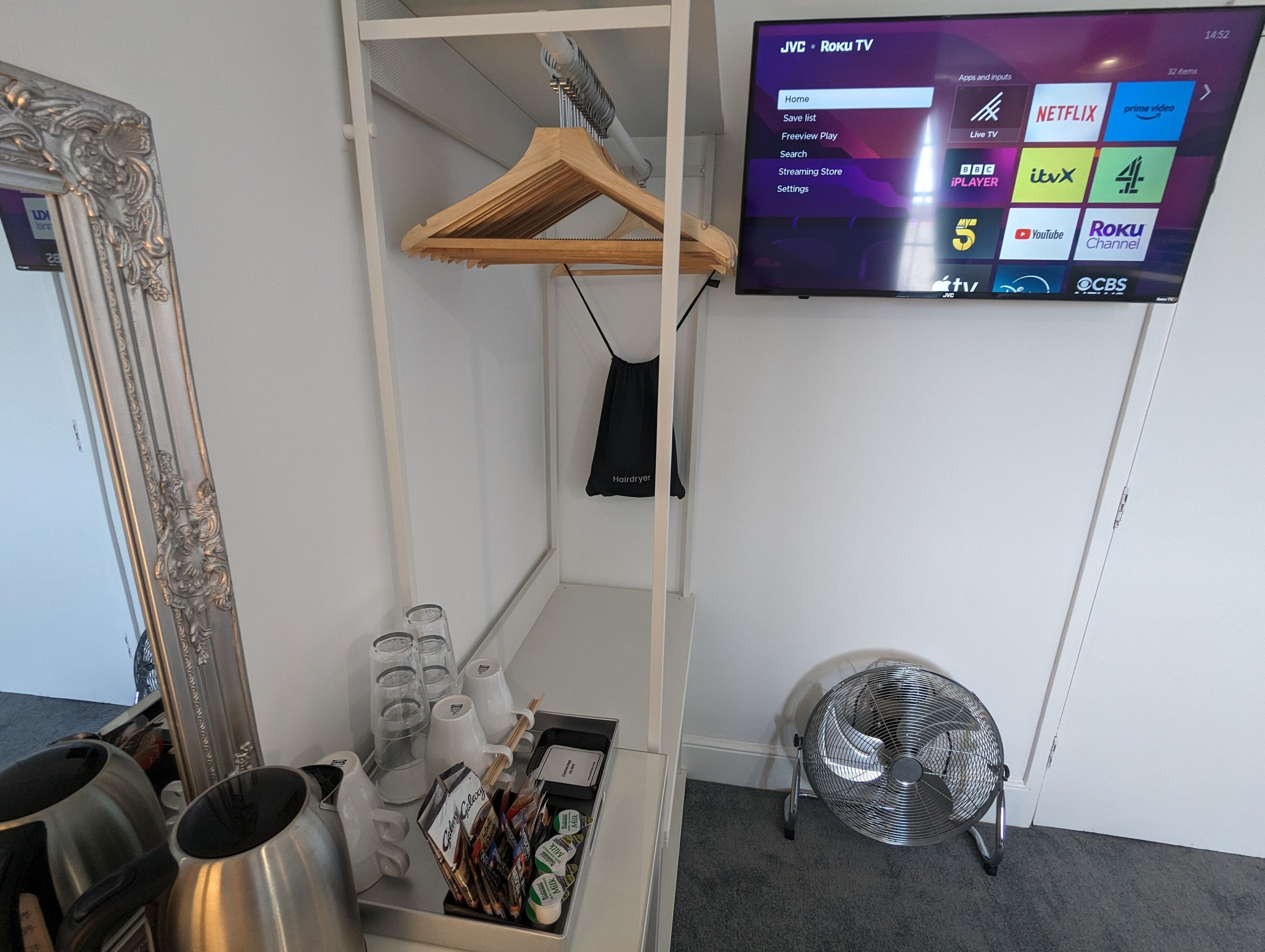 Een kamer met een tv waarop streamingdiensten worden afgespeeld, een spiegel, een ventilator en een plank met diverse spullen.
