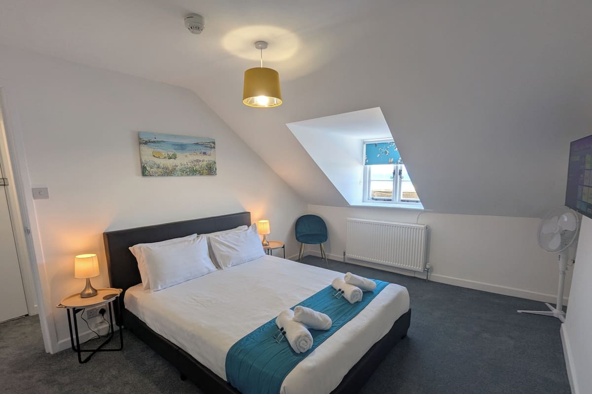 A bedroom with a bed, a desk, a chair, a radiator, a ceiling fan, and a window.