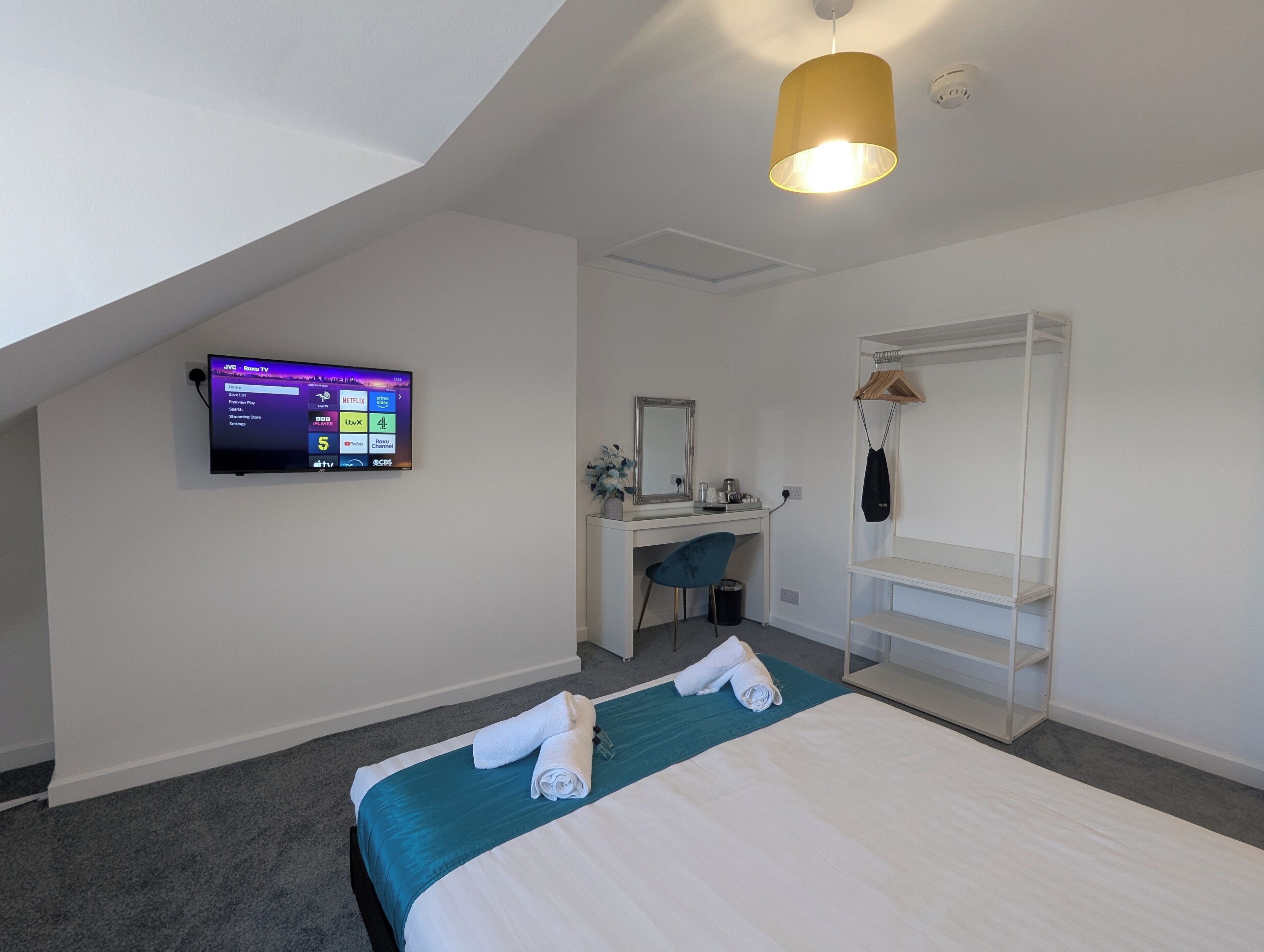 Ein modernes Hotelzimmer mit einem Bett, einem Schreibtisch, einem Stuhl, einem an der Wand befestigten Fernseher und einem Hängehandtuchhalter.