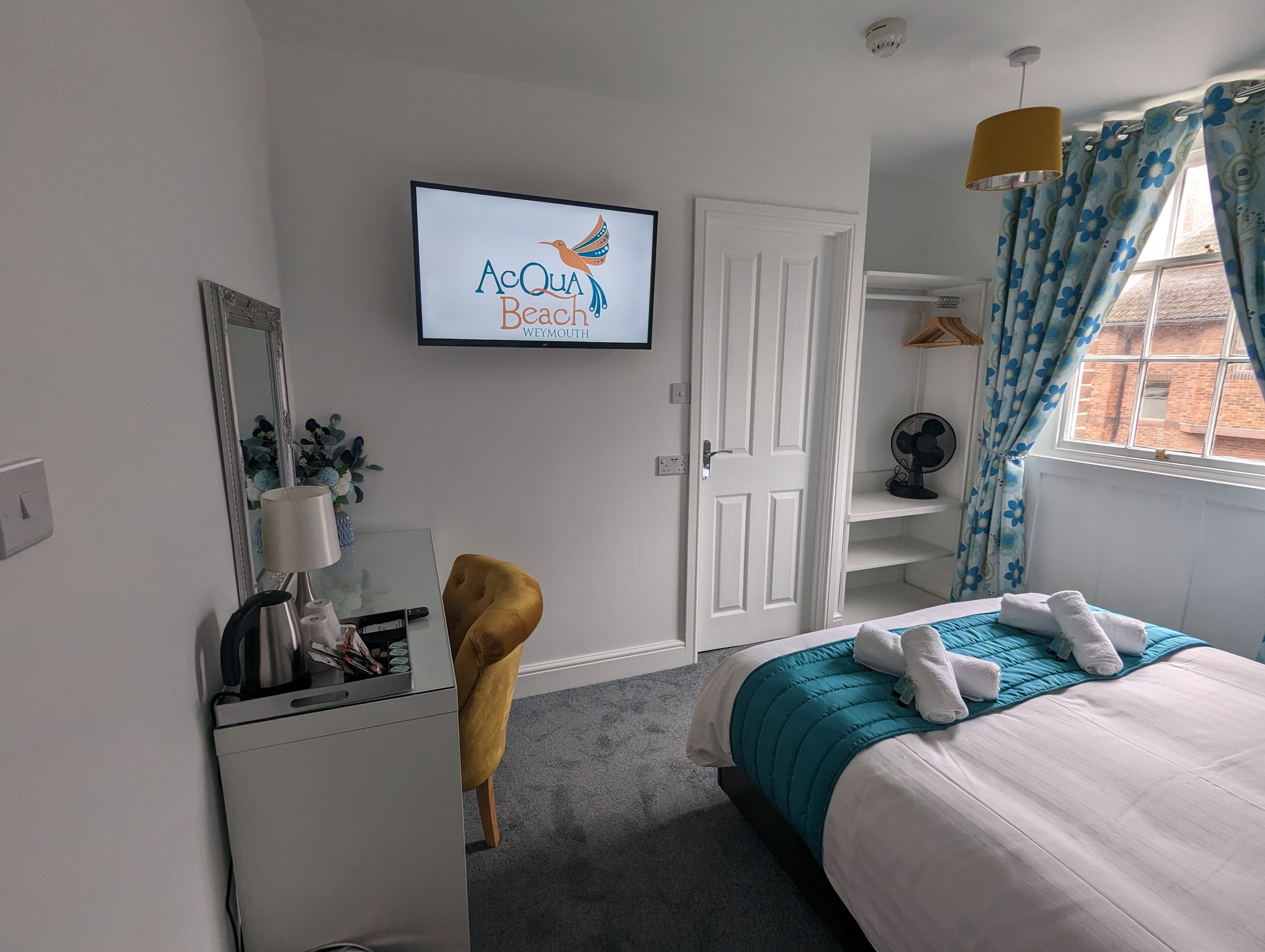 A hotel room with a bed, a desk, a chair, a TV, and a window with curtains.