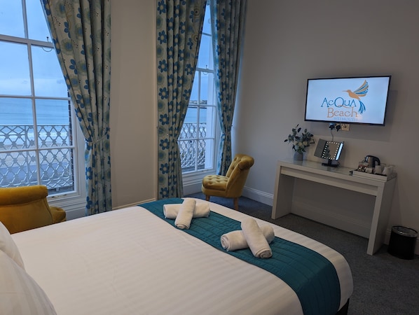 Habitación de hotel con cama, una silla, escritorio con televisor y vista al mar.