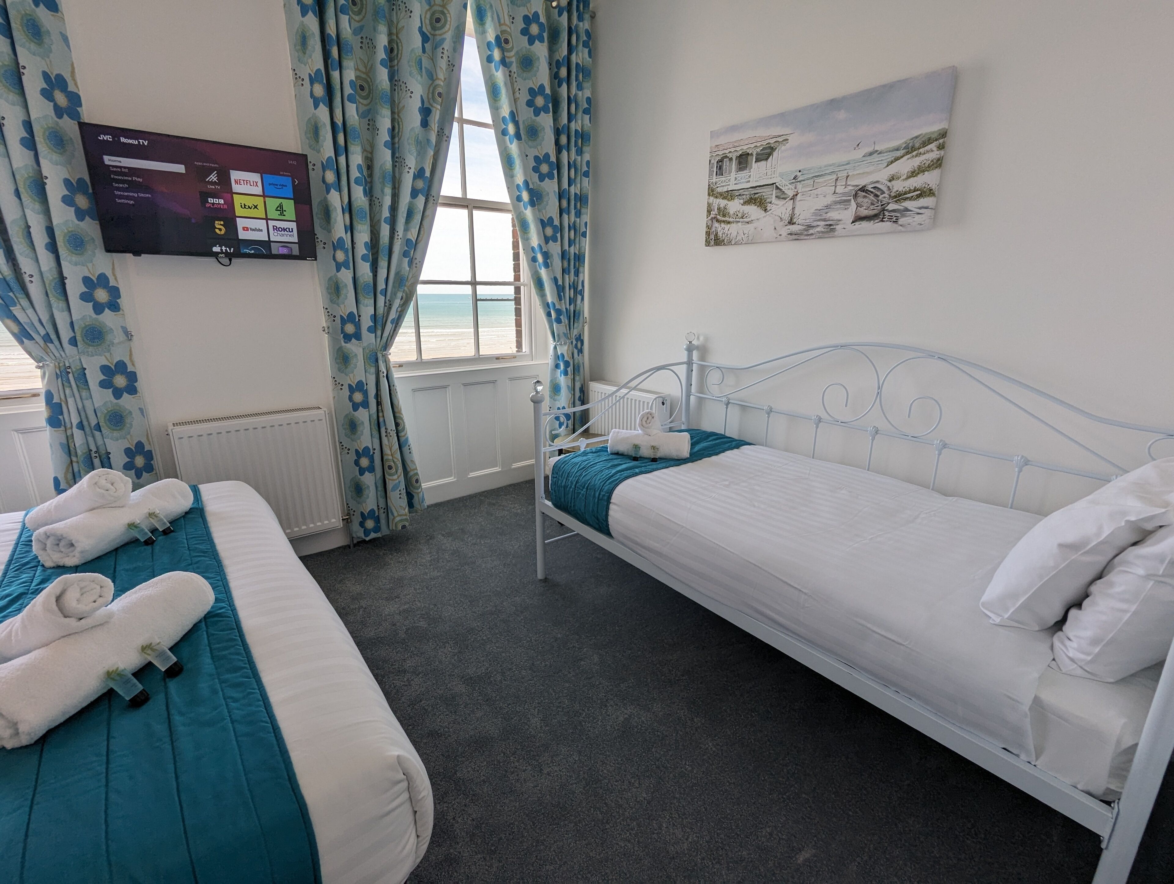 Habitación de hotel con dos camas, un televisor montado en la pared y un cuadro con una playa.