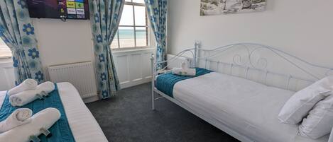 Habitación de hotel con dos camas, un televisor montado en la pared y un cuadro con una playa.