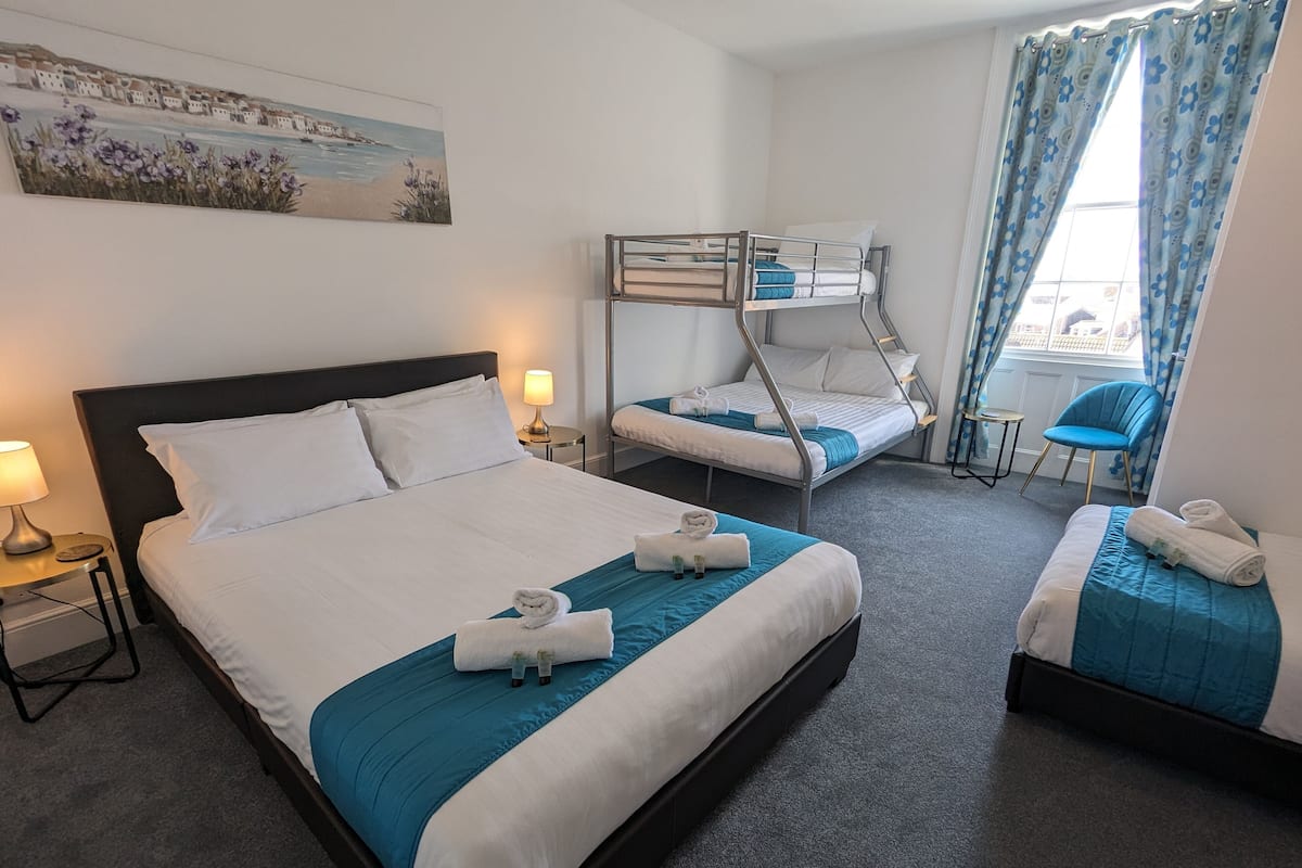 A hotel room with a large bed, a bunk bed, a desk, and a chair.