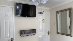 A room with a mounted TV, a large mirror, and a door with a security camera. - Tower Hill Guest House (Basingstoke)