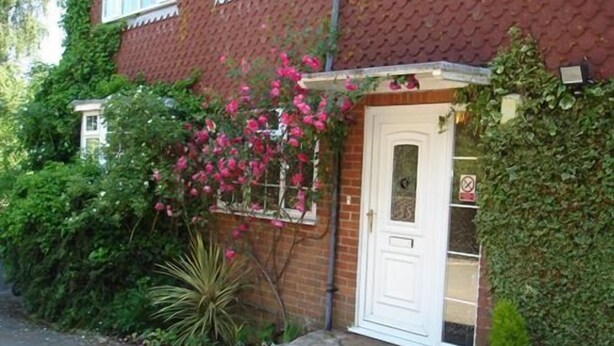 A brick house with a white door, surrounded by lush greenery and pink flowers. - Tower Hill Guest House (Basingstoke)