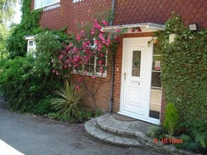 A brick house with a white door, surrounded by lush greenery and pink flowers. - Tower Hill Guest House (Basingstoke)