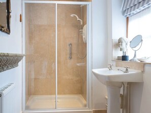 Un baño con ducha envuelta en vidrio, lavamanos sobre pedestal y tocador con espejo.