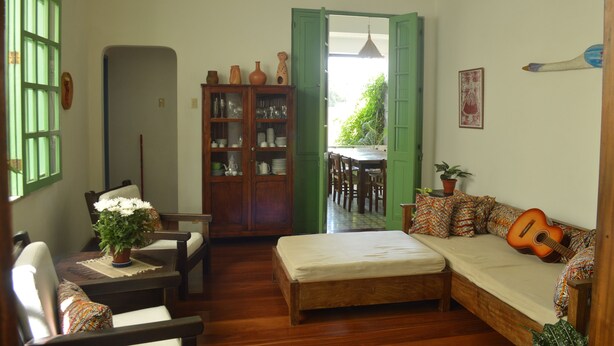 Una habitación acogedora con una cama de madera, un sofá con una guitarra, una mesa de comedor y un aparador con vajilla.
