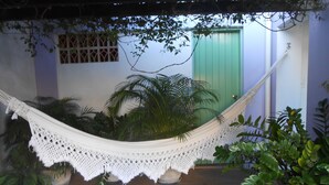 Una hamaca en un patio con plantas en macetas y una puerta verde al fondo.
