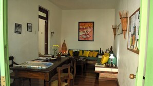 Una sala de estar acogedora con una mesa de comedor de madera, un sofá con cojines y una estantería de pared con adornos.