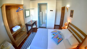 Habitación de hotel con cama, armario de madera, escritorio, silla, mesita y puerta que da al baño.