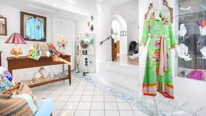 A well-lit room with a mannequin dressed in a colorful floral dress, a wooden console table with decorative items, and a glass display case with jewelry. - Hotel Smeraldo (Praiano)