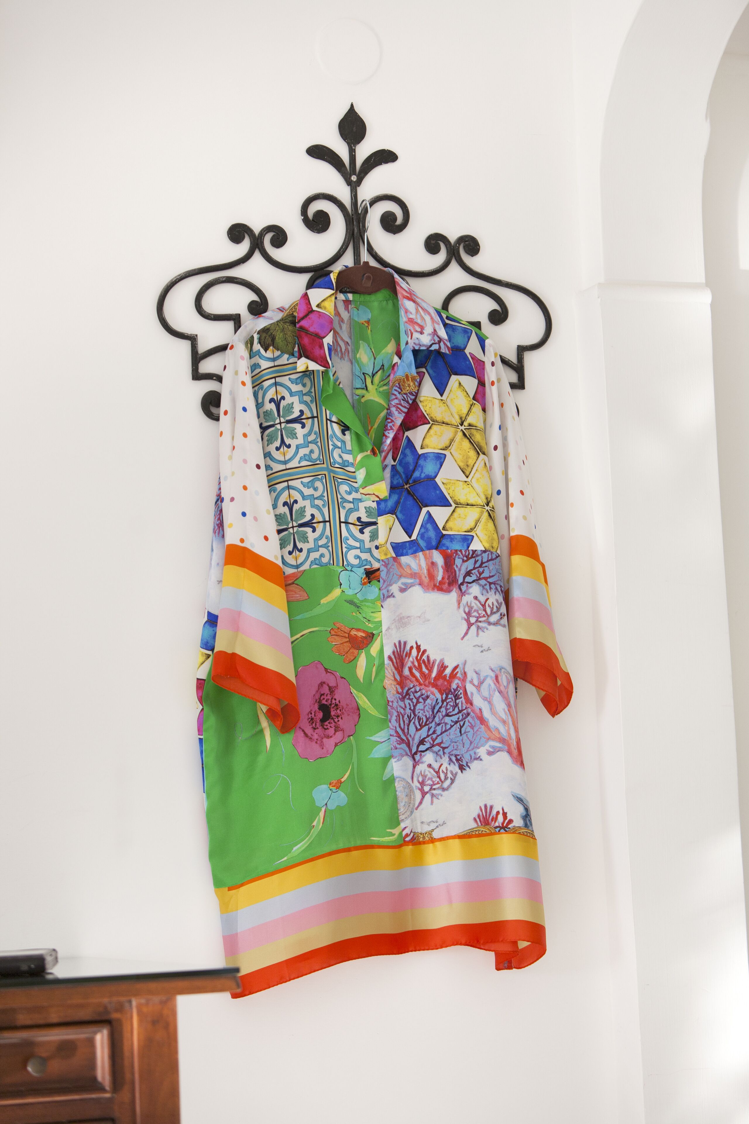 A colorful garment hanging on a black metal stand against a white wall.