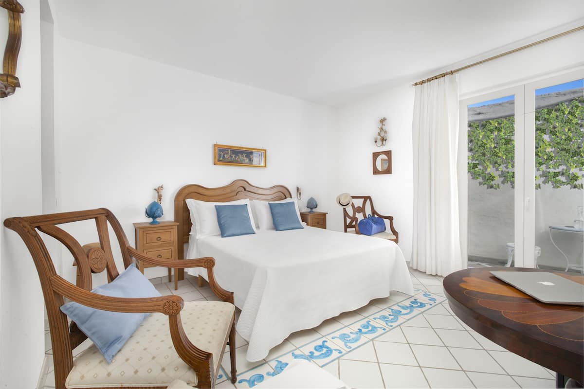 Un dormitorio con cama, dos sillas, una mesa y un ordenador portátil.
