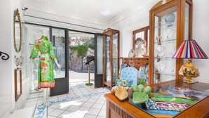A room with a mannequin in a colorful dress, a glass cabinet with decorative items, and a patterned floor. - Hotel Smeraldo (Praiano)