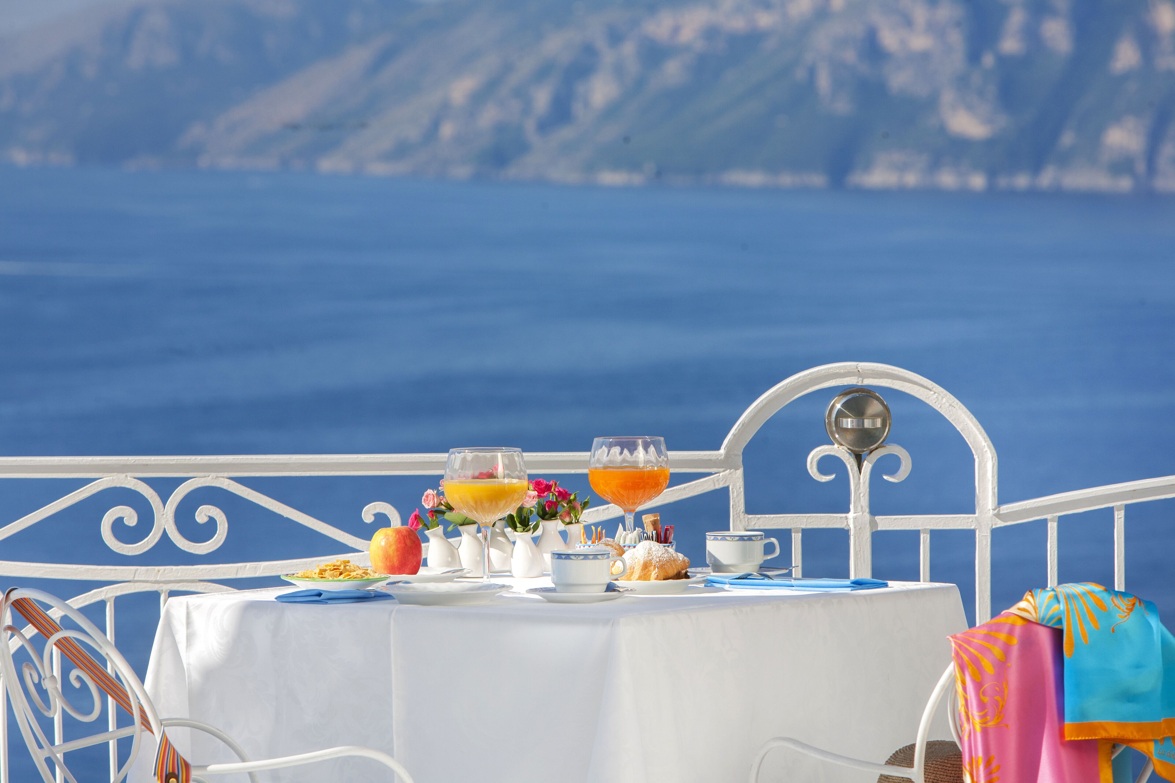 Una mesa servida con alimentos para el desayuno, incluyendo pasteles y bebidas, con vistas a un paisaje marino.